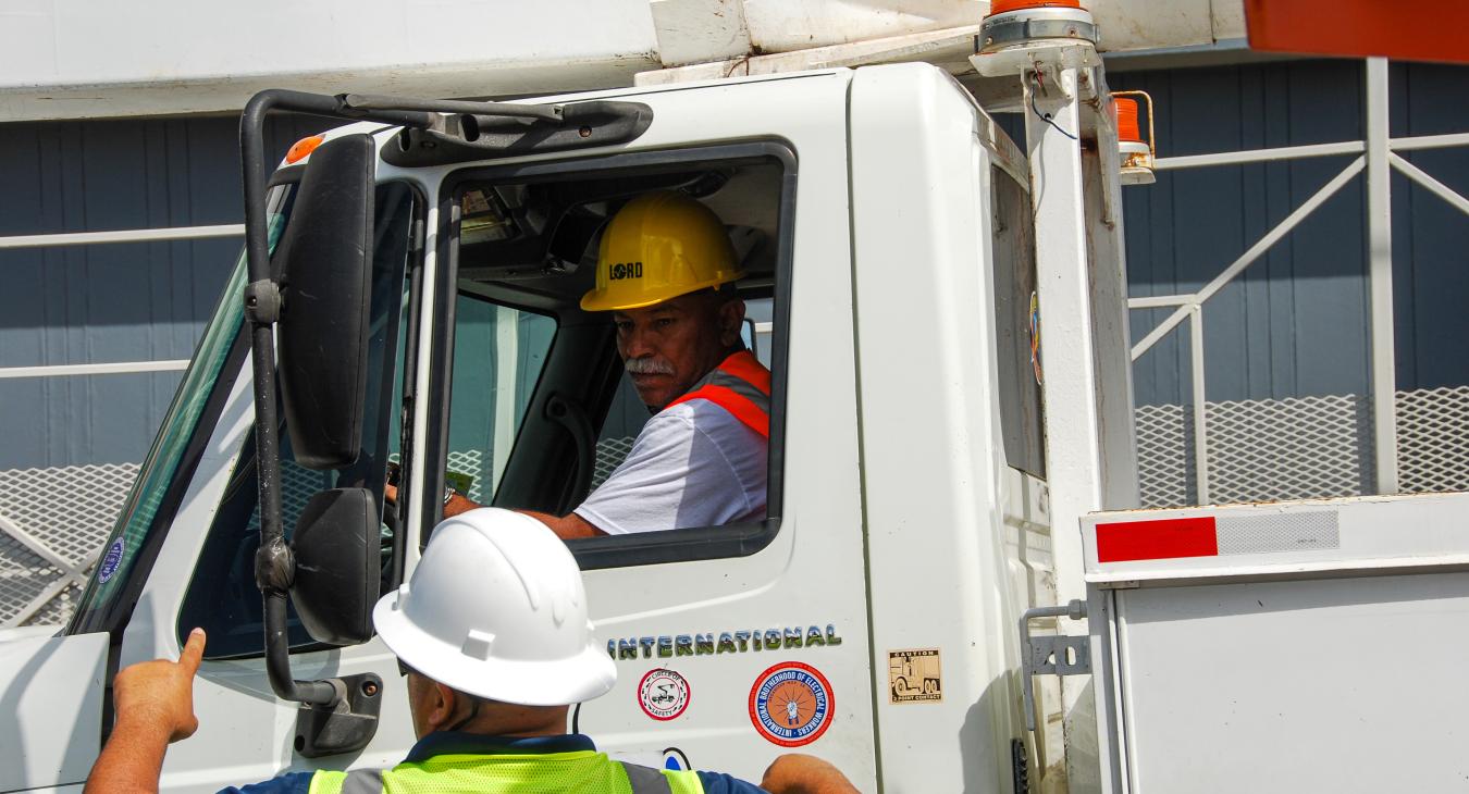 Two men, one driving truck, the other giving instructions